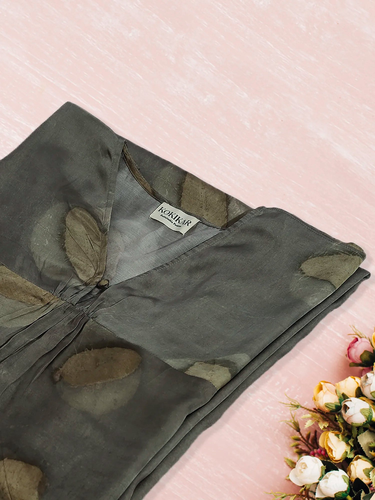 Folded green ecoprinted kaftan with floral patterns on a light pink surface