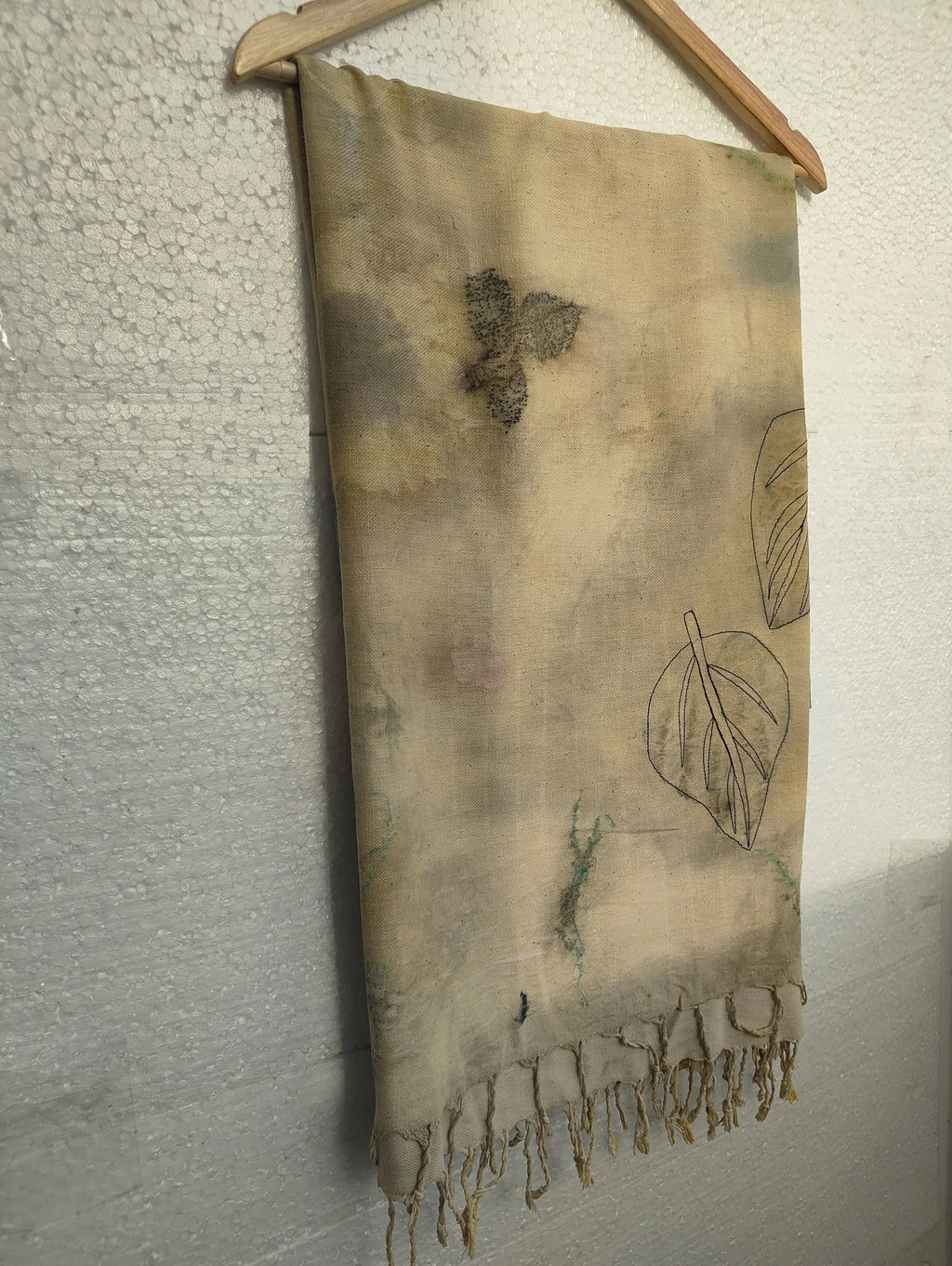 Ecoprinted Ahimsa (Eri) Silk Wrap Scarf with leaf patterns hanging against a textured wall.