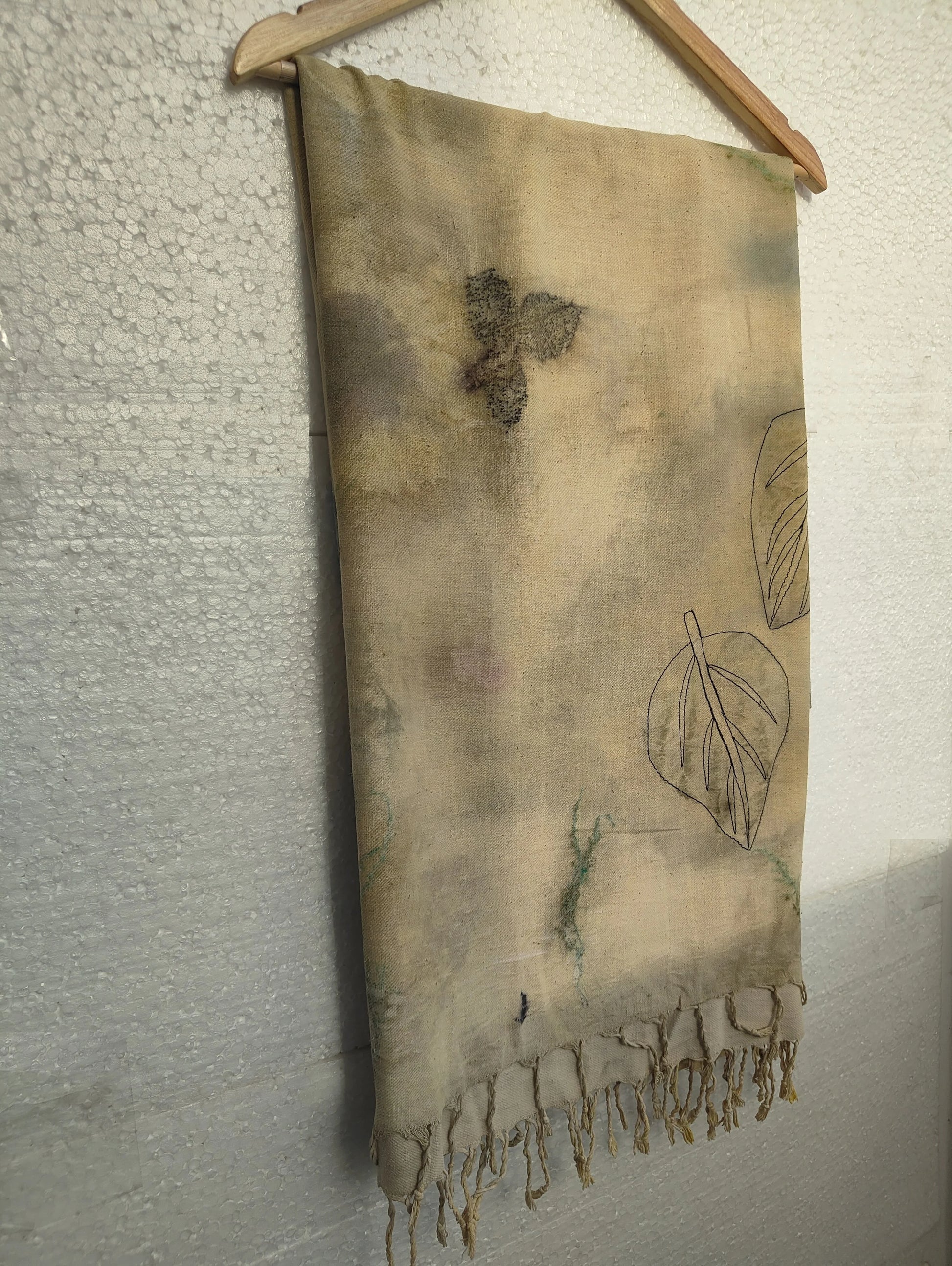 Ecoprinted Ahimsa (Eri) Silk Wrap Scarf with leaf patterns hanging against a textured wall.