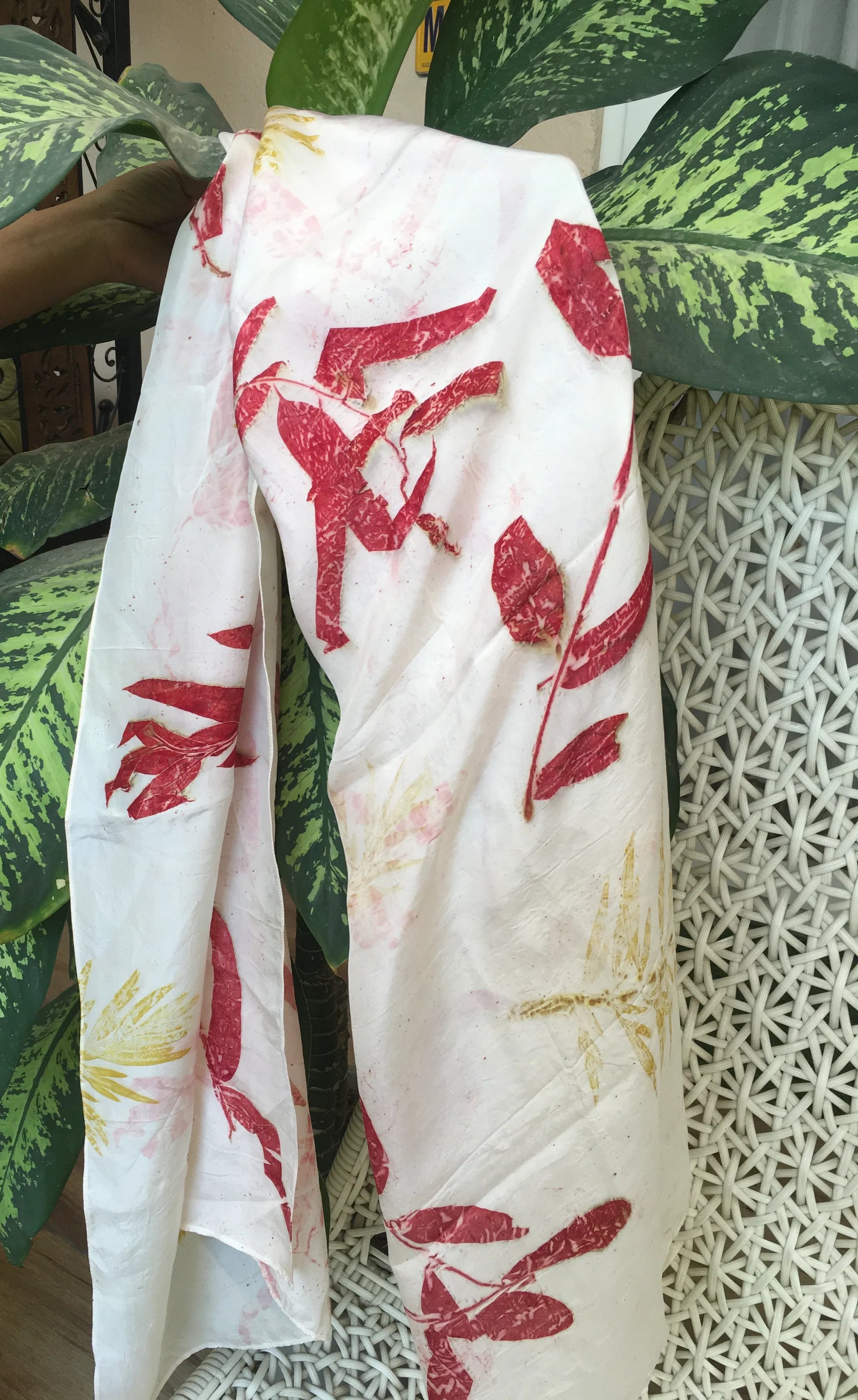 Natural dyed pure silk scarf with red botanical eucalyptus patterns draped over a plant and textured surface