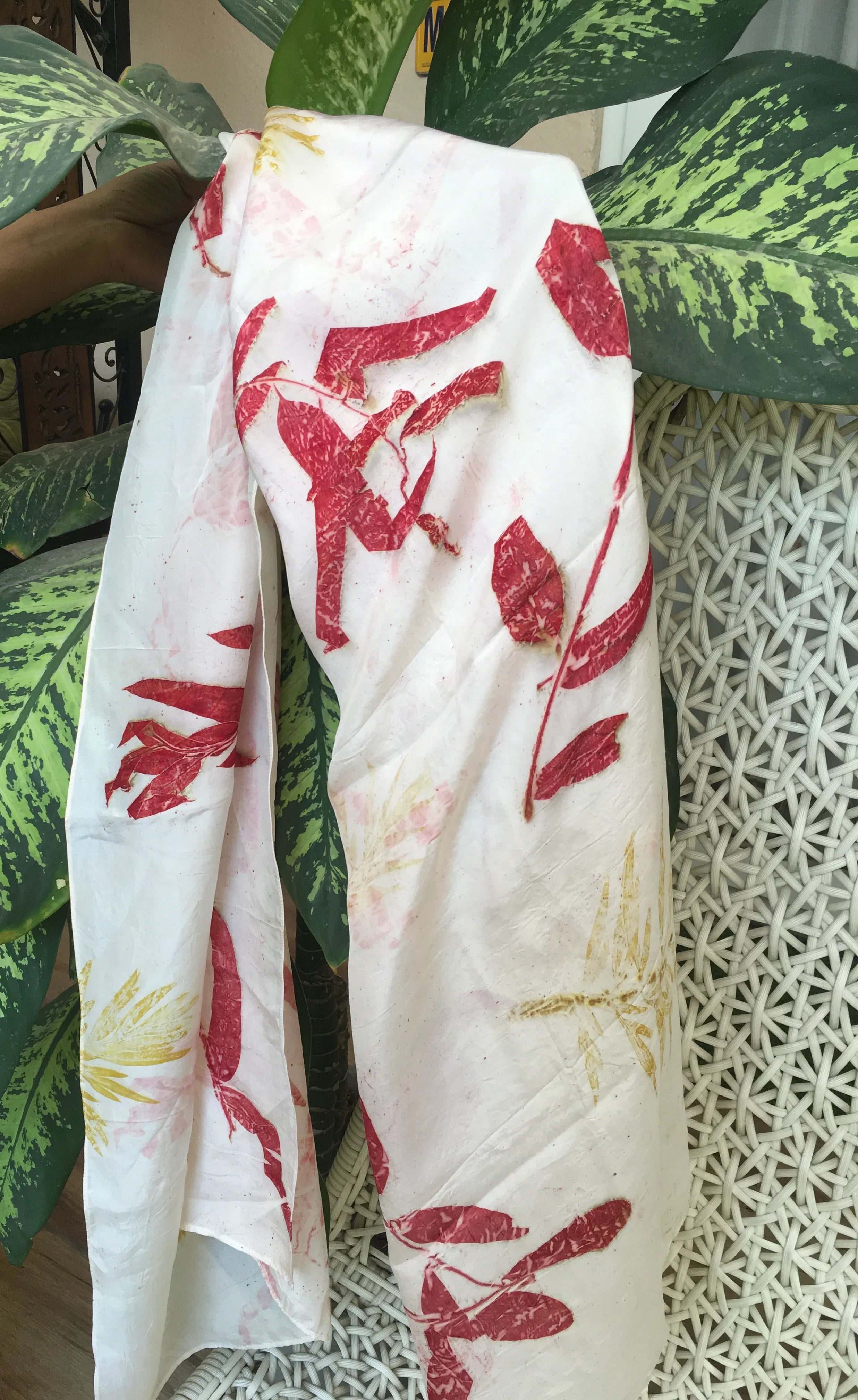 Natural dyed pure silk scarf with red botanical eucalyptus patterns draped over a plant and textured surface