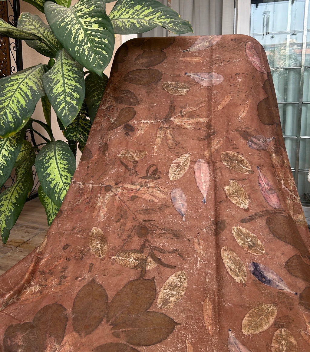 Artisan eco printed silk scarf showcasing mixed botanical leaf prints on naturally dyed dark brown silk in front of a green plant