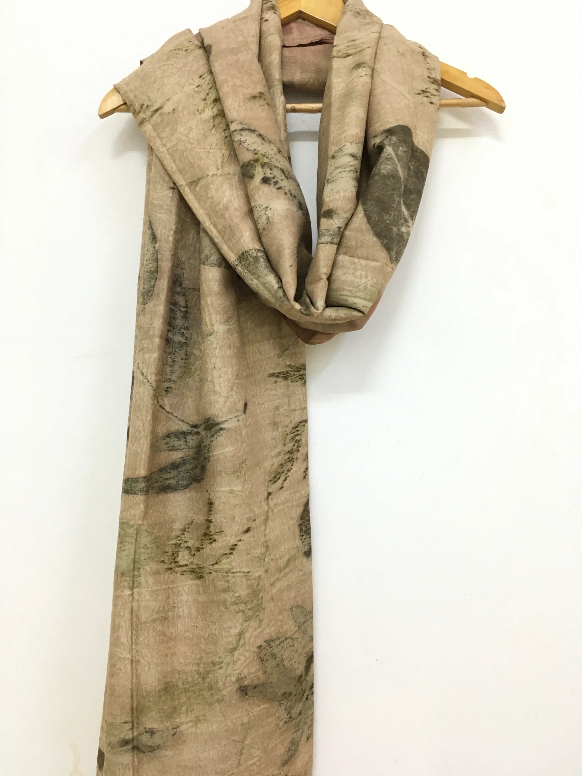 Beige eco printed pure silk scarf with green leaf pattern draped over a wooden hanger on a white background