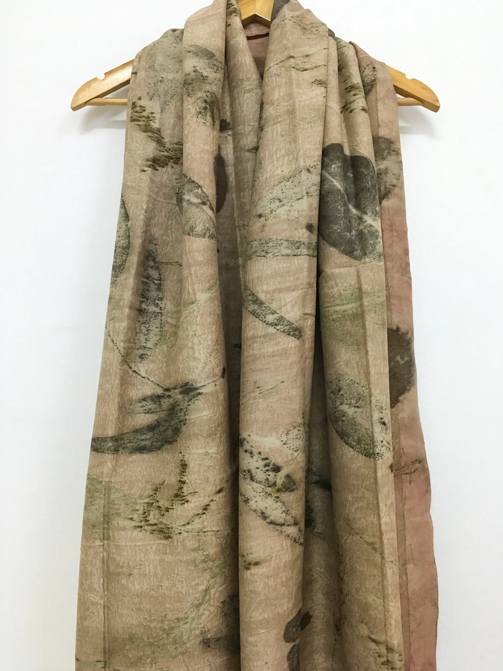Camouflage-patterned eco printed pure silk scarf on a wooden hanger against a white background