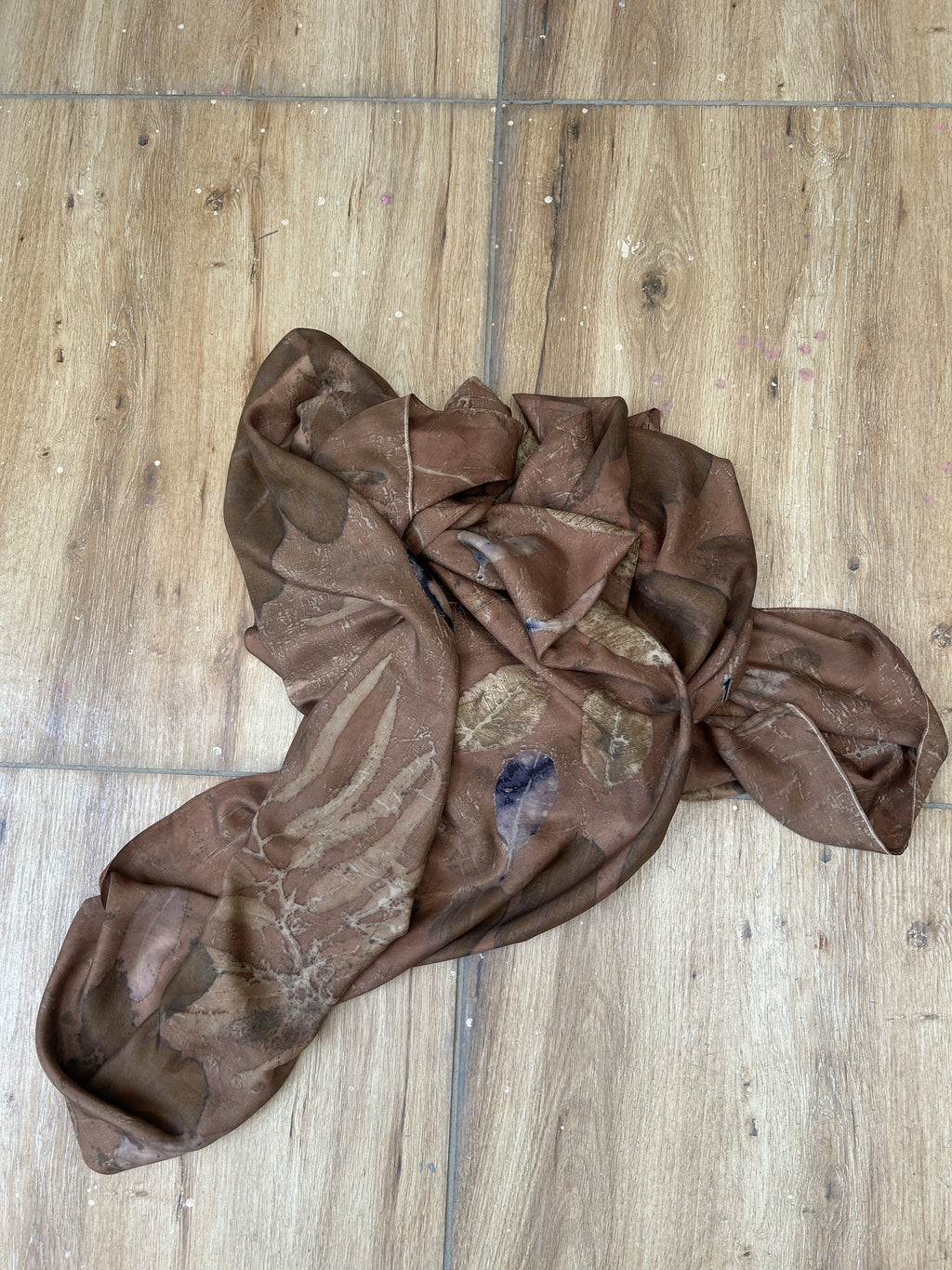 Brown Botanical eco print pure silk scarf with seasonal leaf patterns in earthy brown tones created using natural dyes on a wooden floor
