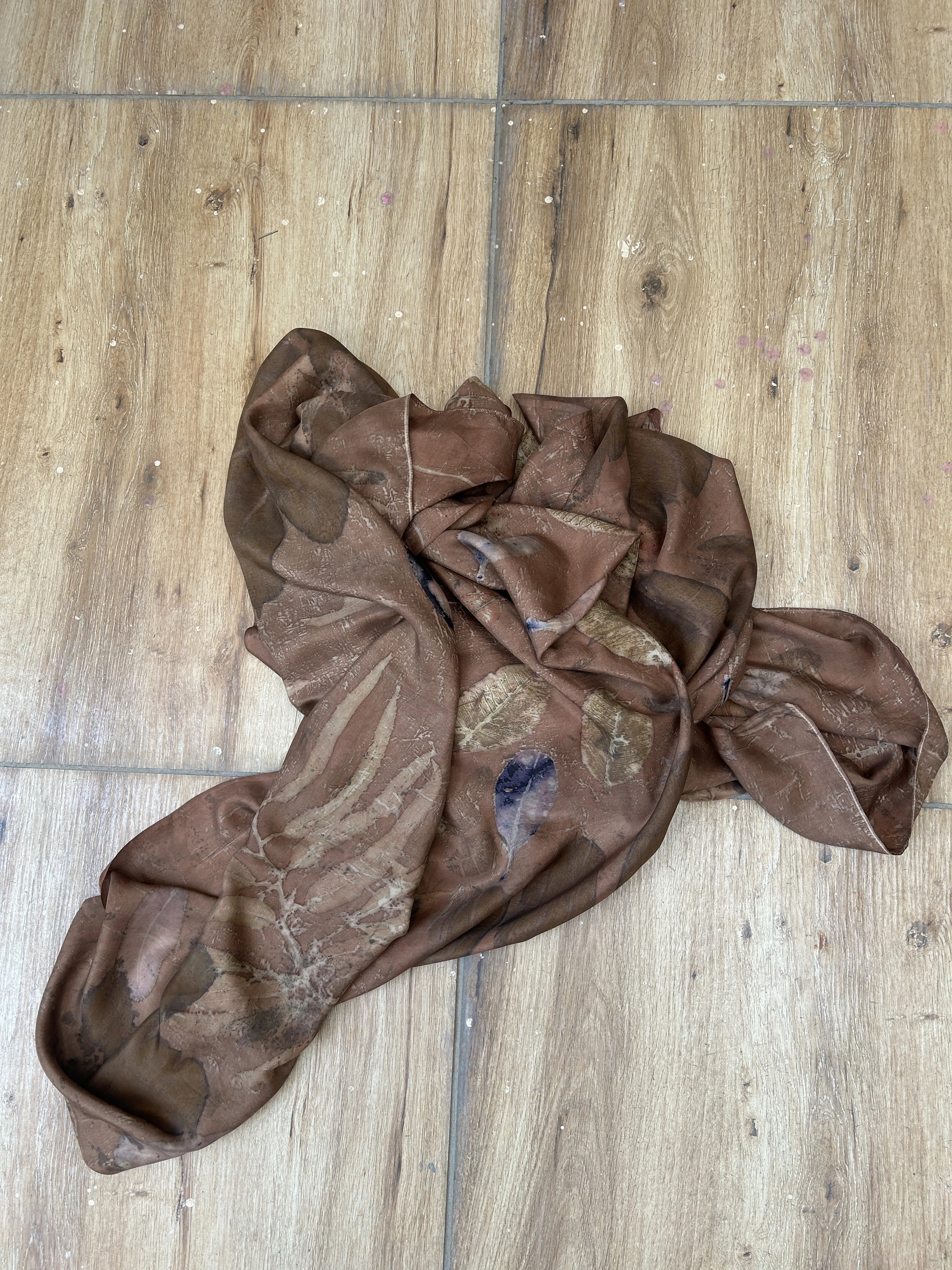 Brown Botanical eco print pure silk scarf with seasonal leaf patterns in earthy brown tones created using natural dyes on a wooden floor