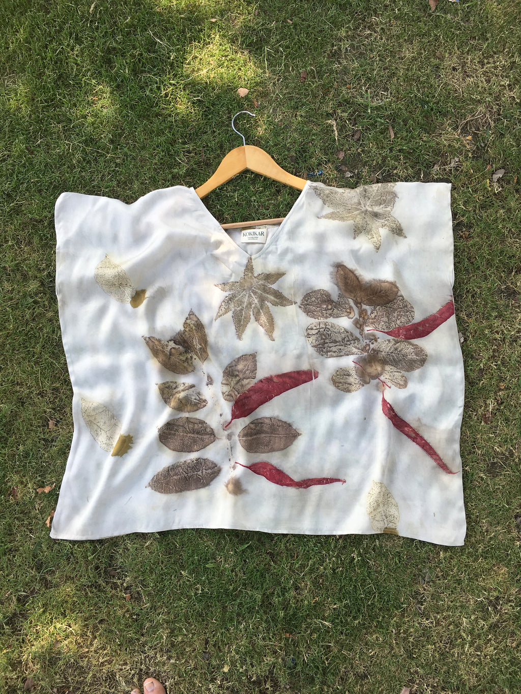 Leaves patterned Kaftan Flared Top on a hanger against a grassy background