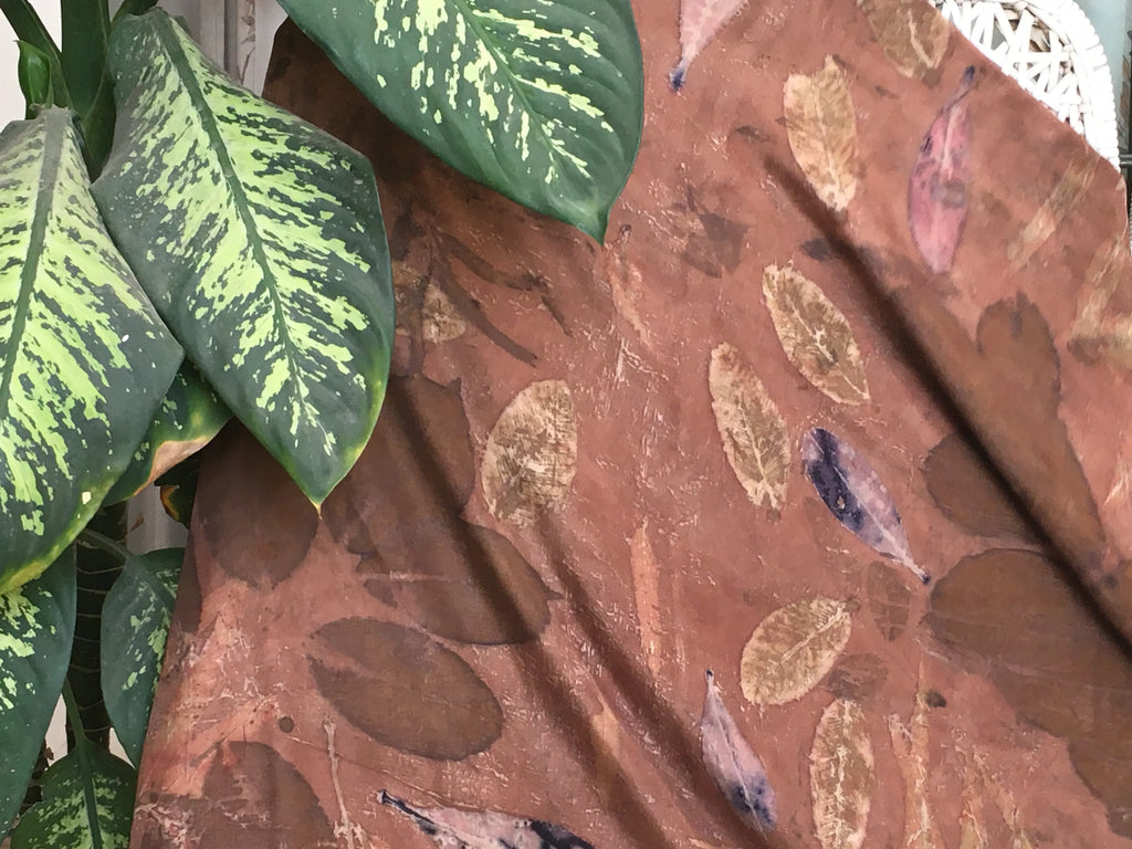 Brown eco printed pure silk scarf with leaf pattern next to green leaves