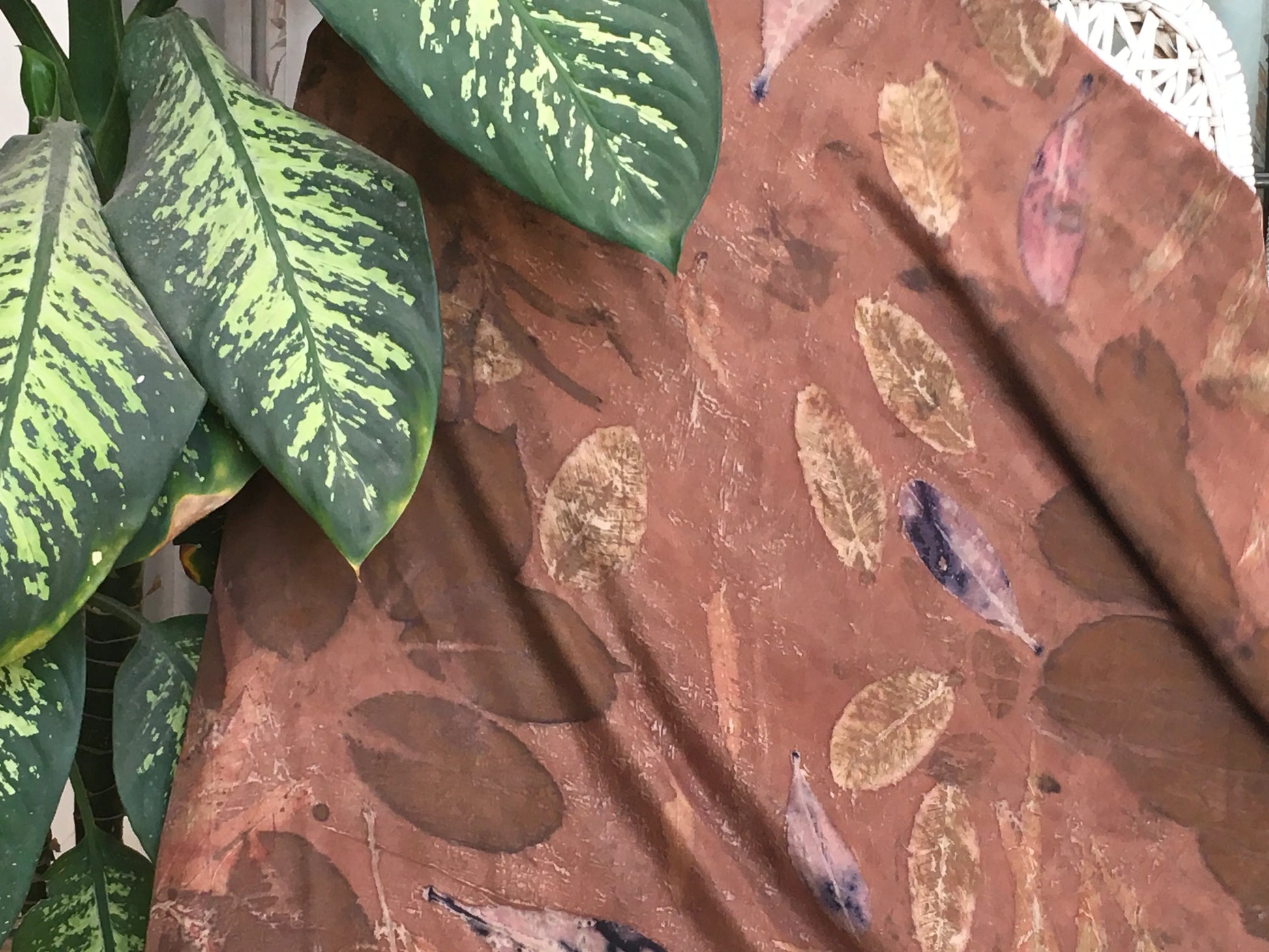 Brown eco printed pure silk scarf with leaf pattern next to green leaves