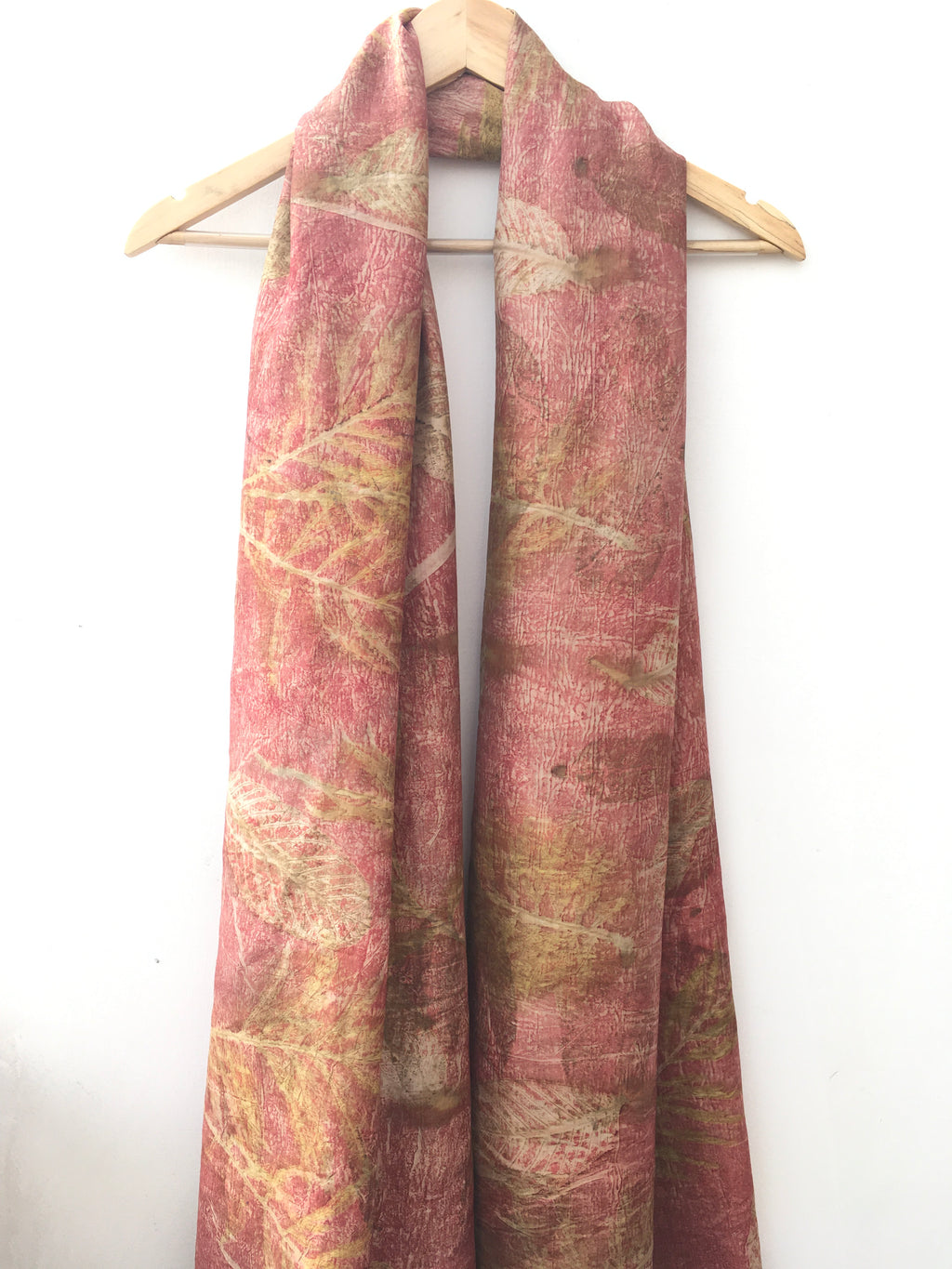 Folded ecoprinted silk scarf with leaves pattern on a white background