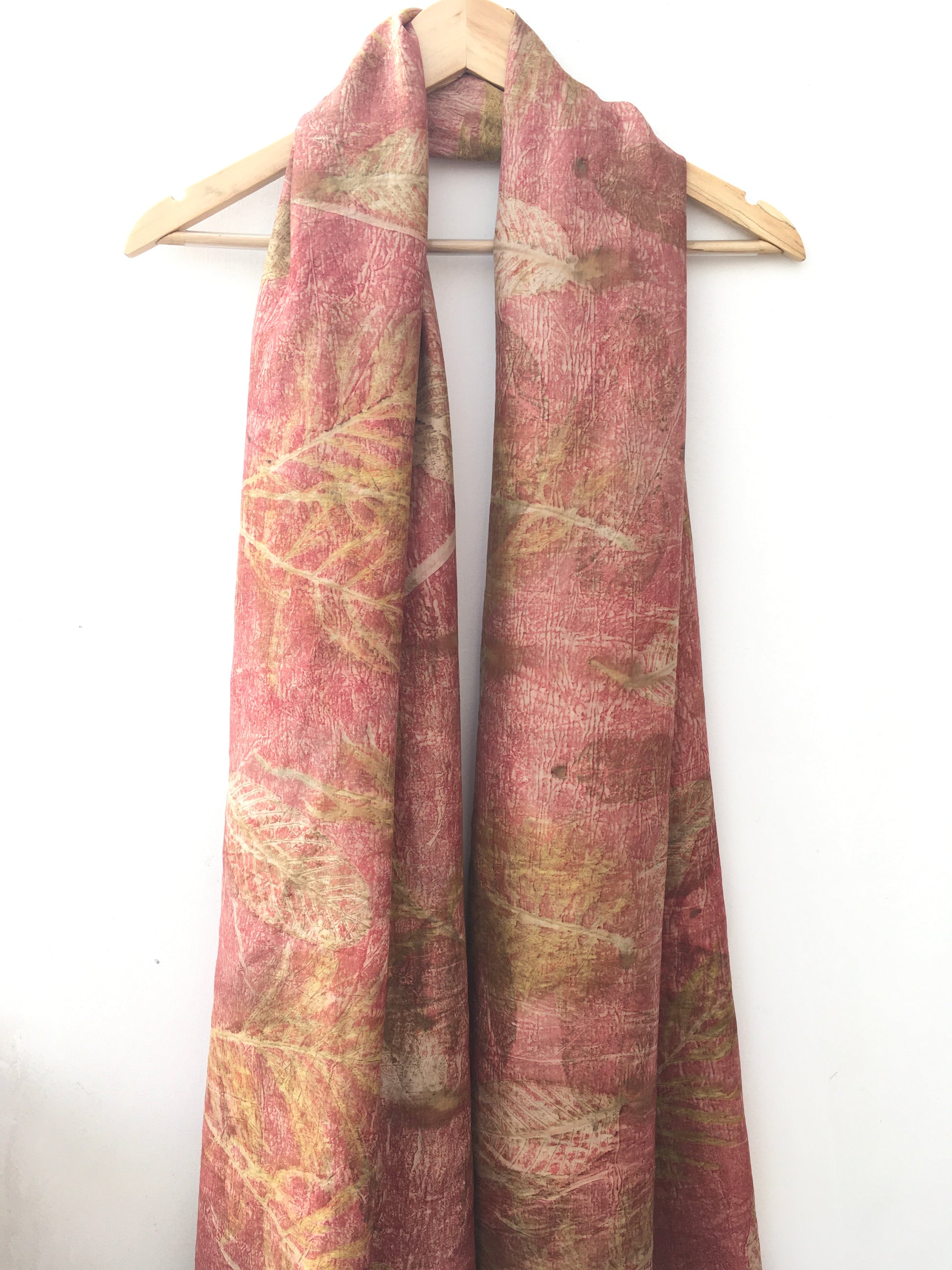Folded ecoprinted silk scarf with leaves pattern on a white background
