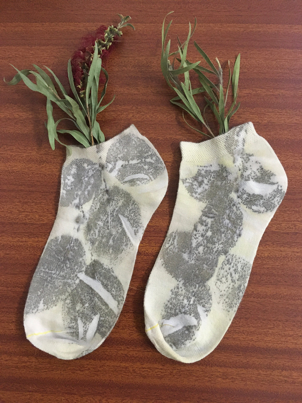 marigold eco printed cotton socks with leaf patterns on a wooden surface with green leaves.