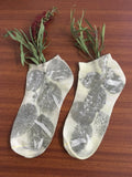 marigold eco printed cotton socks with leaf patterns on a wooden surface with green leaves.