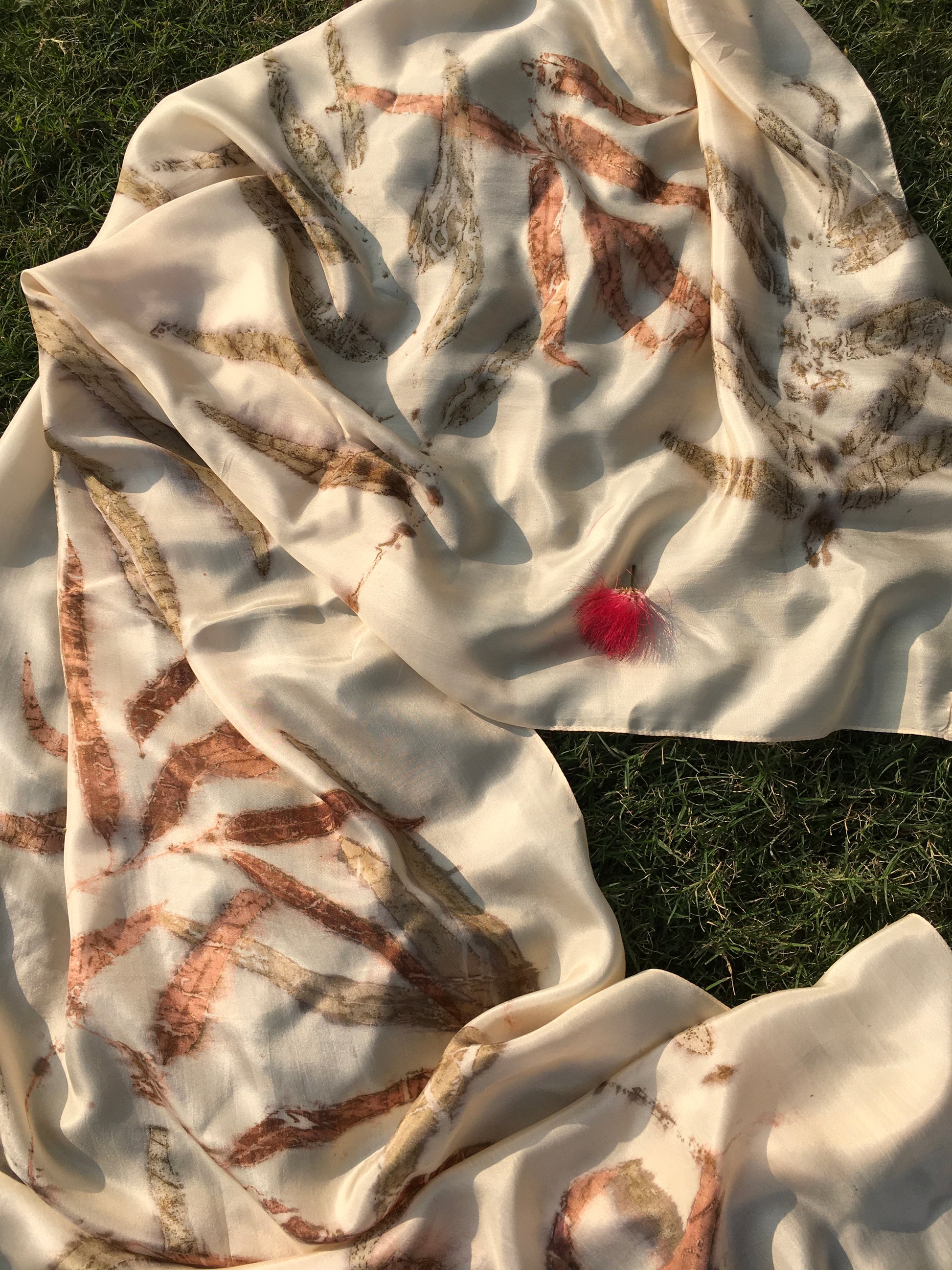 White Ecoprinted pure silk scarf with brown eucalyptus leaves on a grassy background