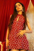 A woman modeling a sleeveless red dress with a white geometric bandhani-style pattern, standing in front of a red curtain backdrop.